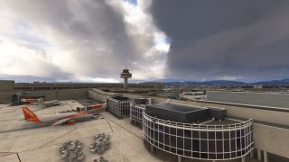 An easyJet airliner sits beside a glass-fronted airport terminal, with a control tower and distant mountains beneath heavy clouds.