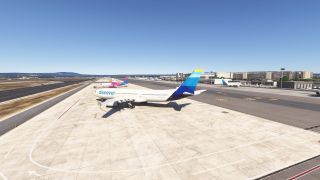 A Discover airliner with a blue and yellow tail sits on the apron, with terminal buildings and other aircraft behind it.