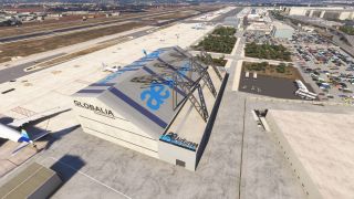 An Air Europa maintenance hangar with exposed roof trusses stands beside parked airliners, airport runways, and crowded car parks.