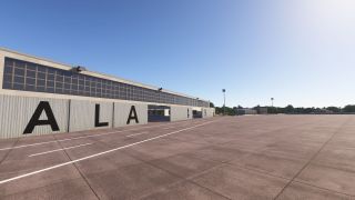 A long hangar marked ALA 49 borders an empty concrete apron with white lines and tall floodlights under clear skies.