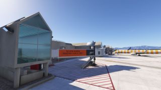 Yellow-and-white Condor aircraft stand beside terminal jet bridges, with red apron markings and mountains visible beneath a clear blue sky.