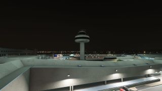 An airport control tower rises above illuminated terminal roofs at night, with parked airliners and distant city lights behind it.