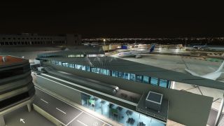 An illuminated airport terminal overlooks parked airliners on a floodlit apron at night, with glass corridors and access roads in the foreground.