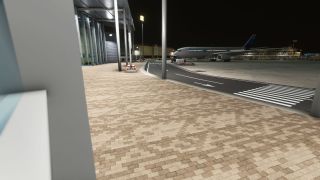 A Discover airliner sits beside an illuminated terminal at night, beyond a marked service road and striped pedestrian crossing.