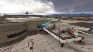 Airliners stand beside terminal jet bridges, with a control tower, ground vehicles, and distant mountains beneath heavy clouds.