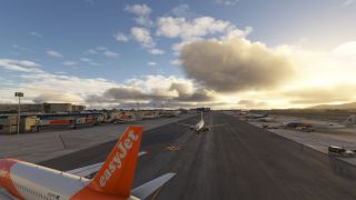 An easyJet aircraft tail dominates the foreground, while airliners line the terminal apron beneath scattered clouds and low golden sunlight.