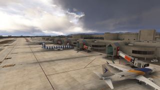 Several passenger jets sit beside numbered terminal gates and jet bridges on a concrete apron beneath dark clouds.