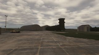 Large black ducts stand beside airport hangars, while a tan pickup truck sits on the concrete apron beneath overcast skies.