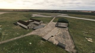 A green open-front hangar and white buildings stand beside a weathered apron, with taxiways extending across the grassy airfield.