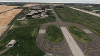 Looping taxiways with yellow markings surround grassy islands, while hangars, a runway, and agricultural fields extend into the distance.