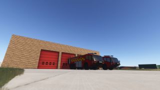 Two red airport fire engines stand outside a brick fire station with red garage doors beneath a clear blue sky.