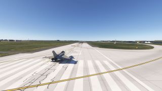 A gray twin-engine fighter jet sits on runway threshold markings, with curved yellow taxiway lines and grassy airfield surroundings.