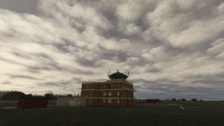 A brick control tower with green trim stands beside fenced equipment and grassy airfield grounds beneath dense, layered clouds.