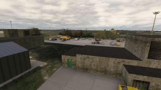 Concrete airport buildings overlook parked cars and a yellow tanker truck, with arched hangars and a control tower beneath cloudy skies.