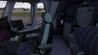 The cockpit contains blue upholstered seats, a sidestick controller, and dark displays, with pavement and airport buildings visible through side windows.