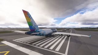 An Airbus A380 with a rainbow-striped tail sits over runway threshold markings, viewed from behind beneath broken clouds.
