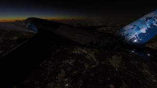 A double-deck airliner with a blue geometric tail flies above illuminated city streets beneath a dark sky and orange horizon.