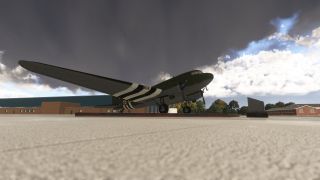 An olive-green twin-engine transport aircraft with black-and-white invasion stripes stands on a raised platform outside brick buildings beneath dark clouds.