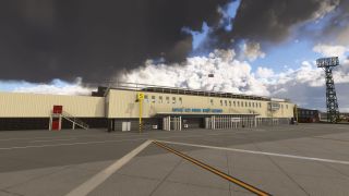 The Royal Air Force Brize Norton terminal faces a marked apron, with yellow stand signs and a floodlight tower beneath dark clouds.