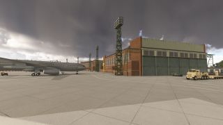A Royal Air Force jet sits beside brick hangars and floodlight towers, with a tan flatbed truck parked beneath dark clouds.