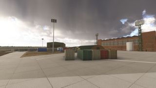 Shipping containers sit on a concrete apron beside brick hangars and tall floodlight towers beneath dark clouds.