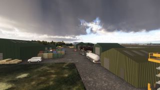 Green corrugated hangars surround a service yard with shipping containers, a white van, and a tanker truck beneath dark clouds.