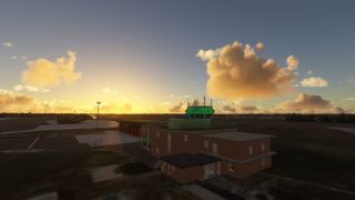 A brick airport control building with green tower windows overlooks taxiways and hangars beneath golden clouds near the horizon.