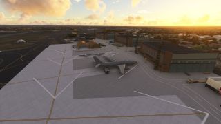 A large gray jet sits on an airport apron beside hangars, smaller aircraft, and service vehicles under a golden sky.