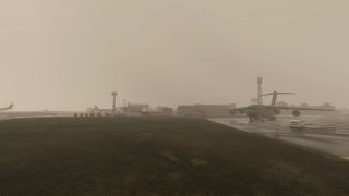 A four-engine military transport aircraft sits on a wet apron beside a white service van, with airport buildings obscured by haze.