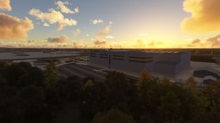A large airport hangar stands beside an empty parking lot, with parked airliners beyond and golden clouds above the tree-lined foreground.