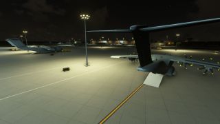 A four-engine turboprop transport sits with its rear cargo ramp lowered on a floodlit apron at night, near other parked aircraft.