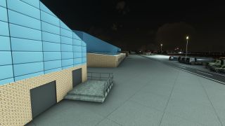 Blue-clad brick airport buildings stand beside a floodlit service road, with tanker trucks parked in a row at night.