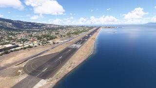 Runway 22 extends along a narrow coastline, with blue water on one side and densely built green hills on the other.