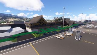 An airport terminal with steep pitched roofs and green covered walkways faces an apron with mobile boarding stairs and ground vehicles.