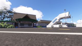 Mobile passenger stairs stand outside the Tahiti Faaa terminal, which features a steep pitched roof, green entrance canopy, and surrounding tropical plants.