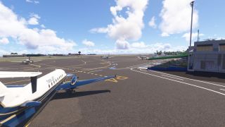 A blue-and-white Twin Jet turboprop sits on a marked airport apron beside a terminal with a green-covered walkway.
