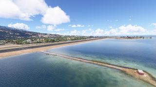 A coastal runway borders blue water and hillside neighborhoods, with a red-and-white antenna hut on a narrow strip of land.