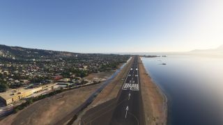 A small aircraft sits near runway 22’s threshold, with coastal water to the right and buildings covering hills to the left.