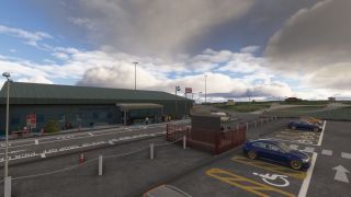An airport terminal with a green roof faces taxi lanes and accessible parking spaces, with people gathered near the entrance.