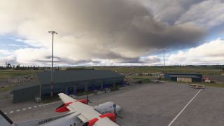 A white twin-engine turboprop with red nacelles sits beside a green-roofed airport terminal beneath thick clouds.