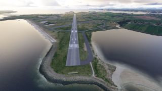 Runway 18 extends along a narrow coastal peninsula, with connecting taxiways, nearby hangars, and water on both sides.