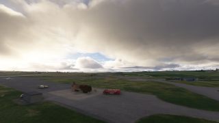A red airport fire truck stands beside a rusted aircraft fuselage on a paved apron beneath heavy clouds.