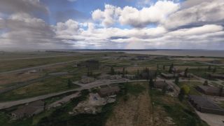 An airport borders a broad body of water, with scattered buildings, paved roads, and a faint rainbow beneath layered clouds.