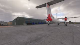A white twin-engine turboprop with red maple leaf markings sits outside a green airport terminal beneath cloudy skies.