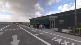 Passengers stand beside luggage carts outside an airport terminal, with marked taxi bays, a yellow car, and a pedestrian crossing nearby.