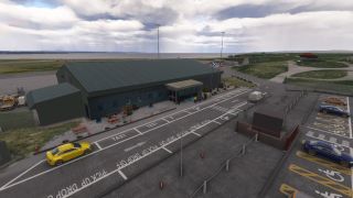 A green-roofed airport terminal stands beside marked taxi bays, accessible parking spaces, and a yellow car, with water beyond the airfield.
