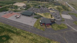 An aerial view shows parked propeller aircraft beside airport buildings, with marked taxiways, car parks, and fire engines outside a fire station.