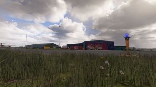 Two fire engines sit outside an airport fire station, with a blue taxiway light and tall grass in the foreground.