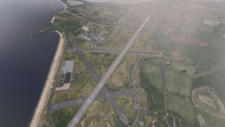 A coastal airport has intersecting runways, taxiways marked with white crosses, and hangars beside a sandy shoreline and surrounding fields.