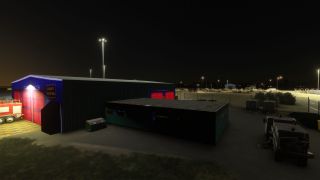 An airport service building has illuminated red garage doors, with a fire engine and street sweeper parked outside at night.